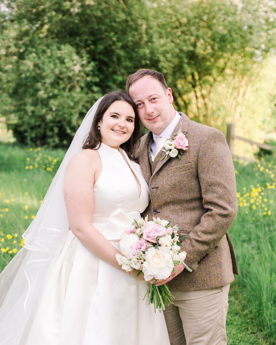 Wedding portraits in a spring meadow with soft natural lighting and pink flowers.