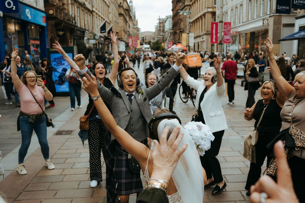 Celebratory crowd gathers on a busy shopping street with people holding phones and taking photos.