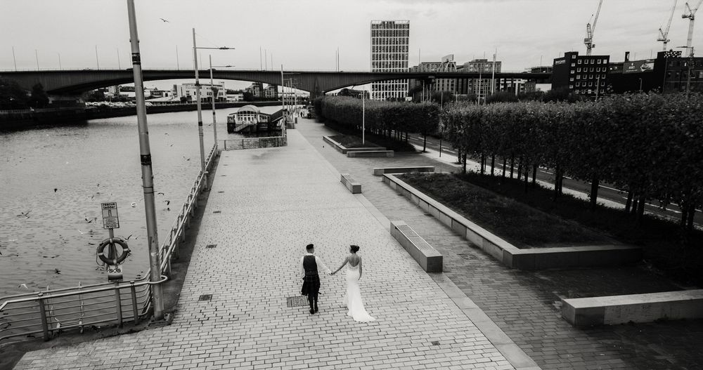A black and white aerial view of a waterfront promenade with two people walking near a harbor and control tower.