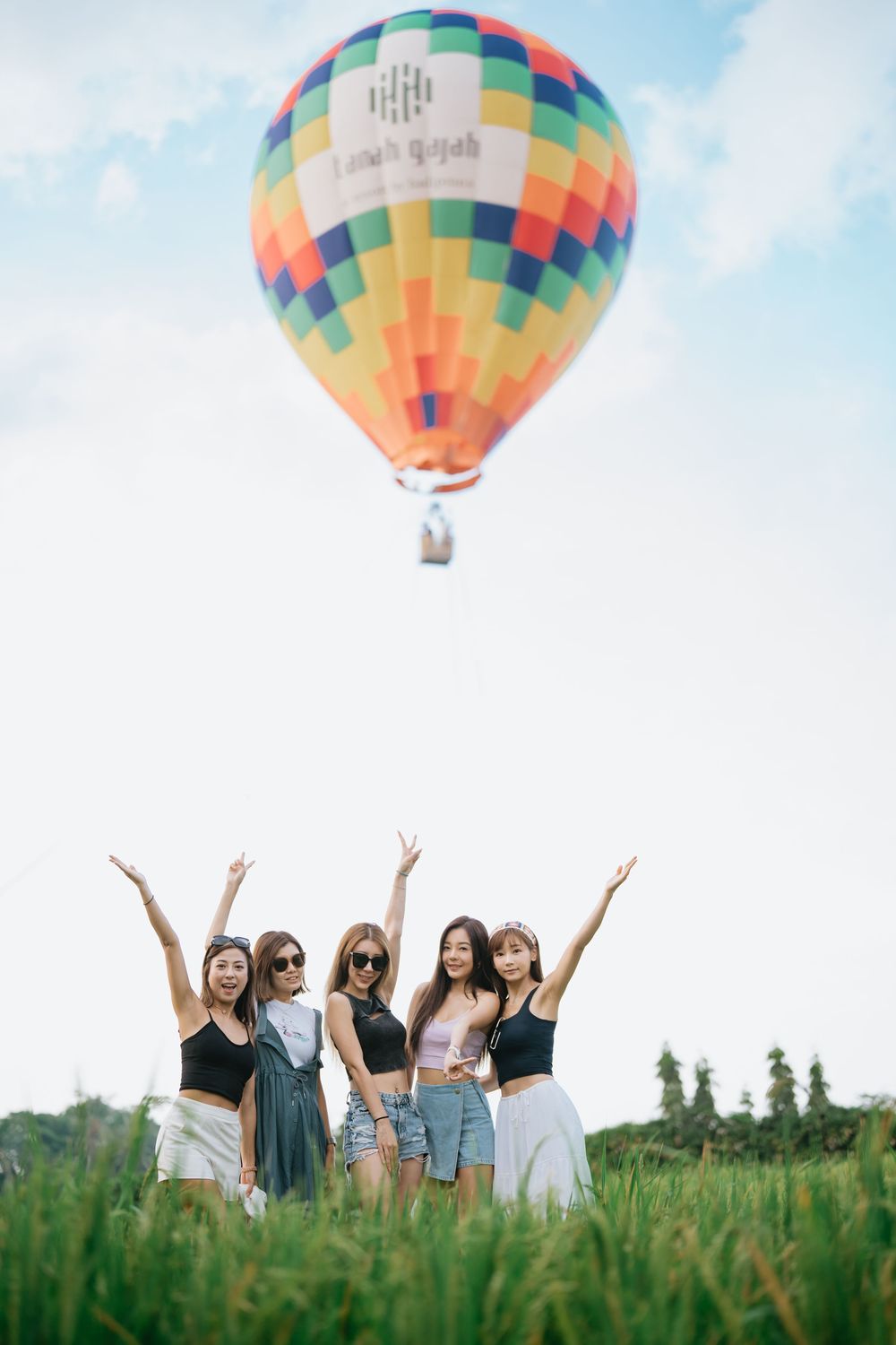 People in casual attire standing in green field beneath colorful hot air balloon.