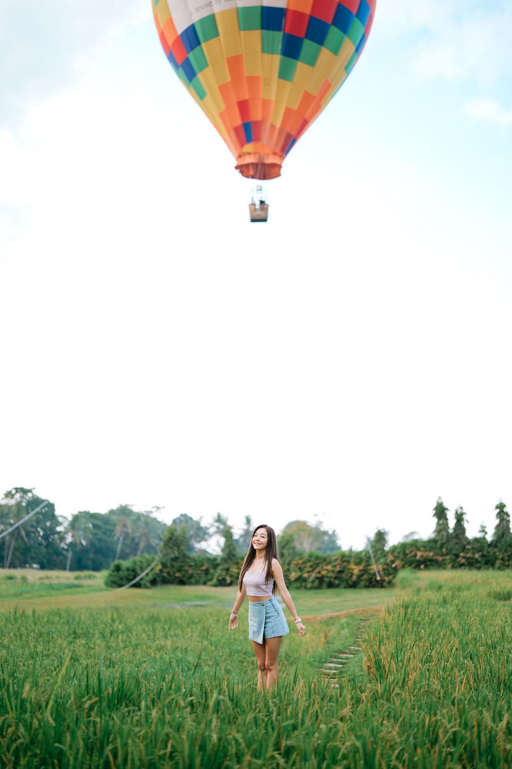 Hot air balloon floating above person standing in verdant countryside field.