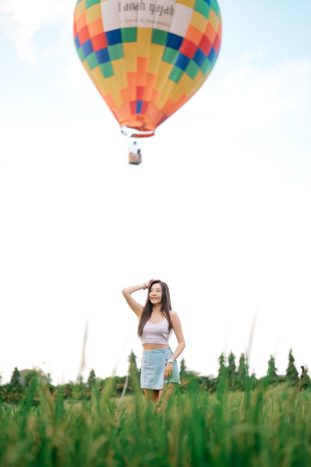 Colorful hot air balloon hovering over person posing in green field.