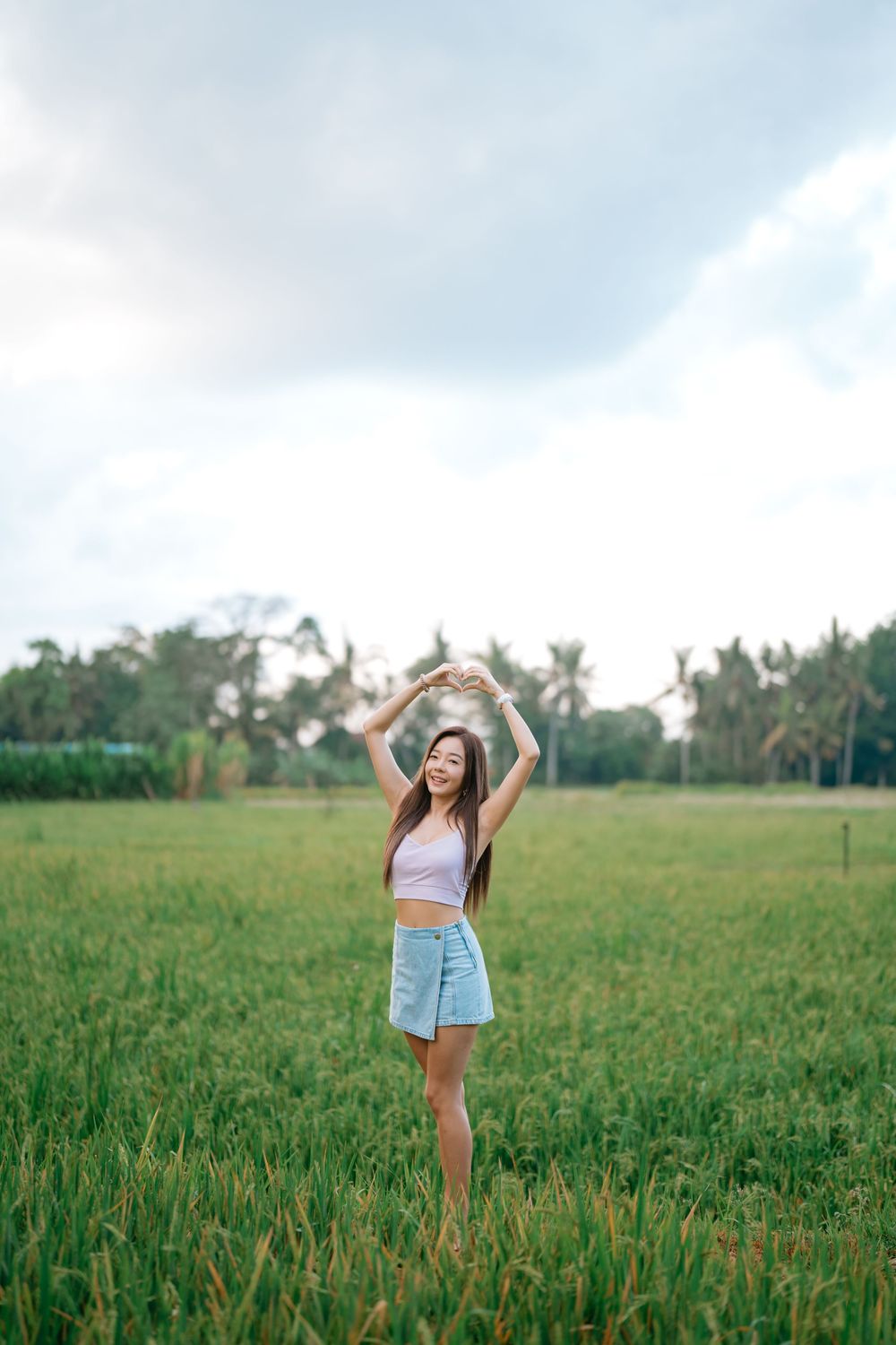 Person in casual summer outfit celebrating with arms raised in grassy field.