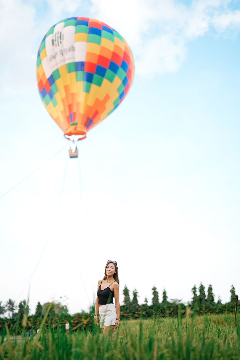 Colorful hot air balloon floating over a green field on a sunny day.