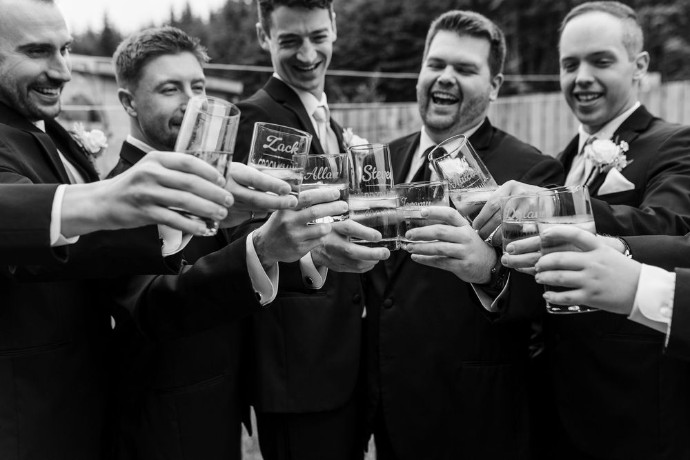A black and white candid photo series showing groomsmen toasting and clinking glasses in celebration during a wedding.