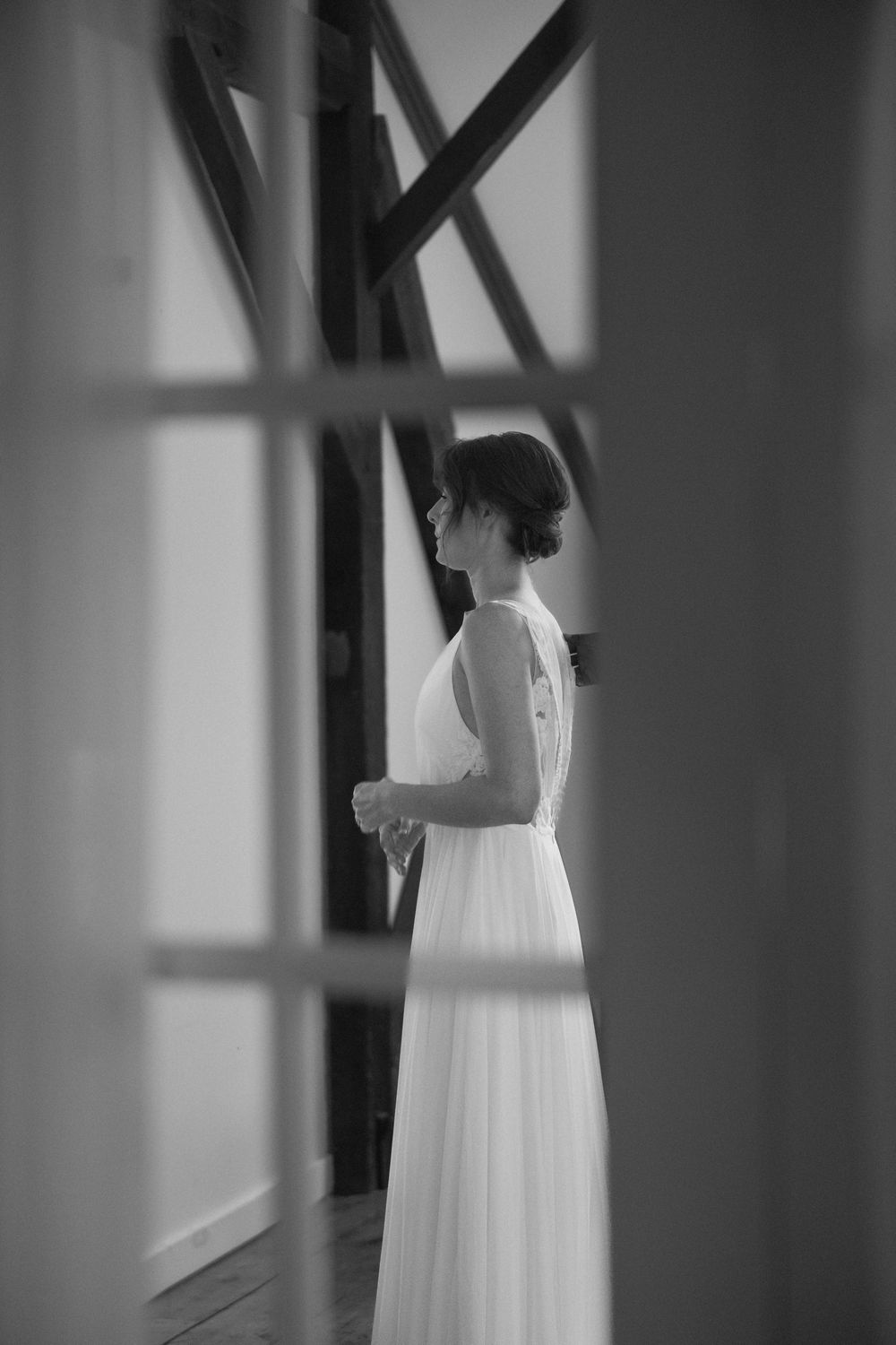 Artistic black and white photo of bride in flowing dress through window frame.