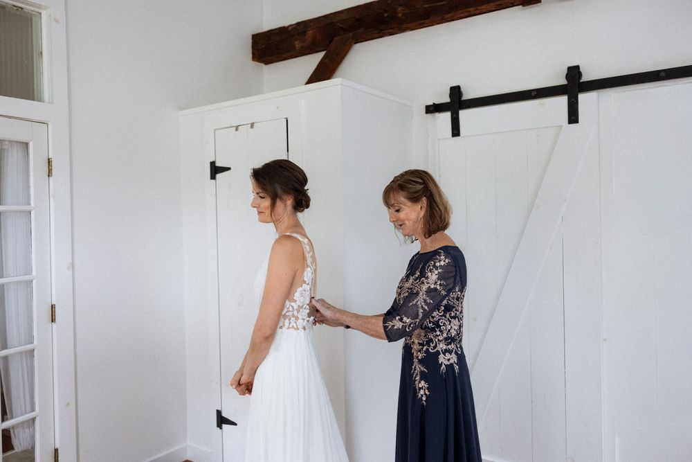 Wedding dress preparation scene in a rustic white room with exposed wooden beams.