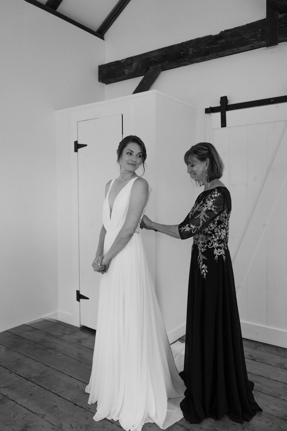 Black and white image of wedding dress fitting in room with rustic wooden beams.