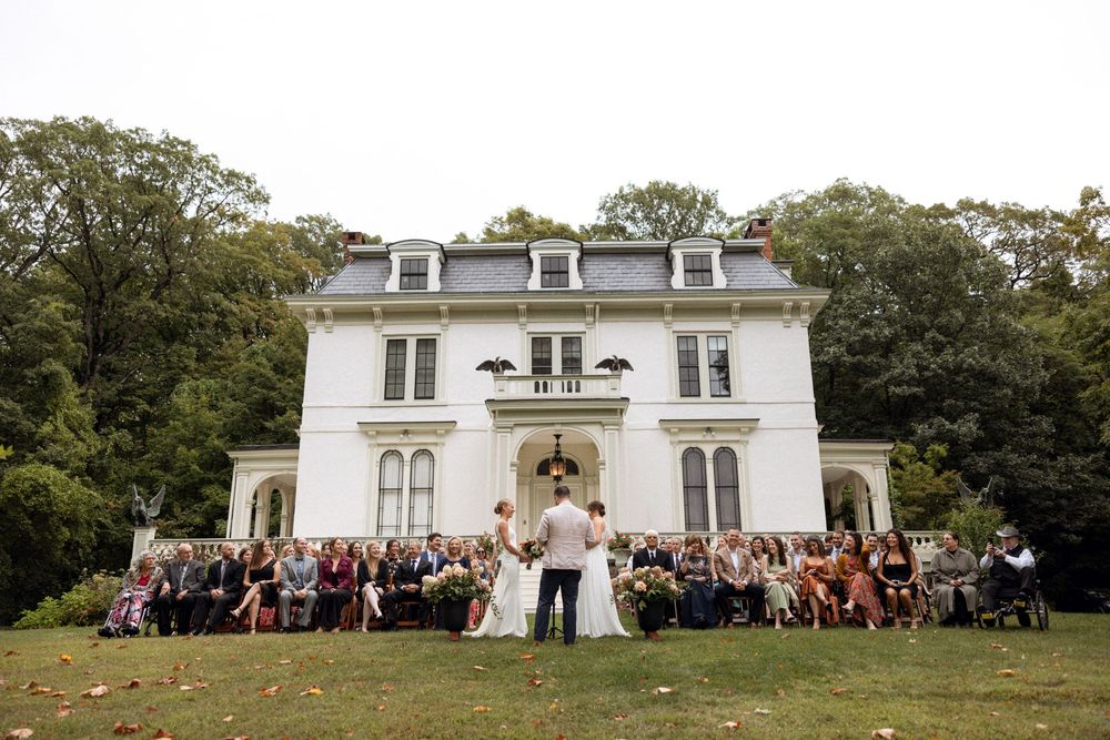 Panoramic view of a white wedding venue with guests gathered outside.