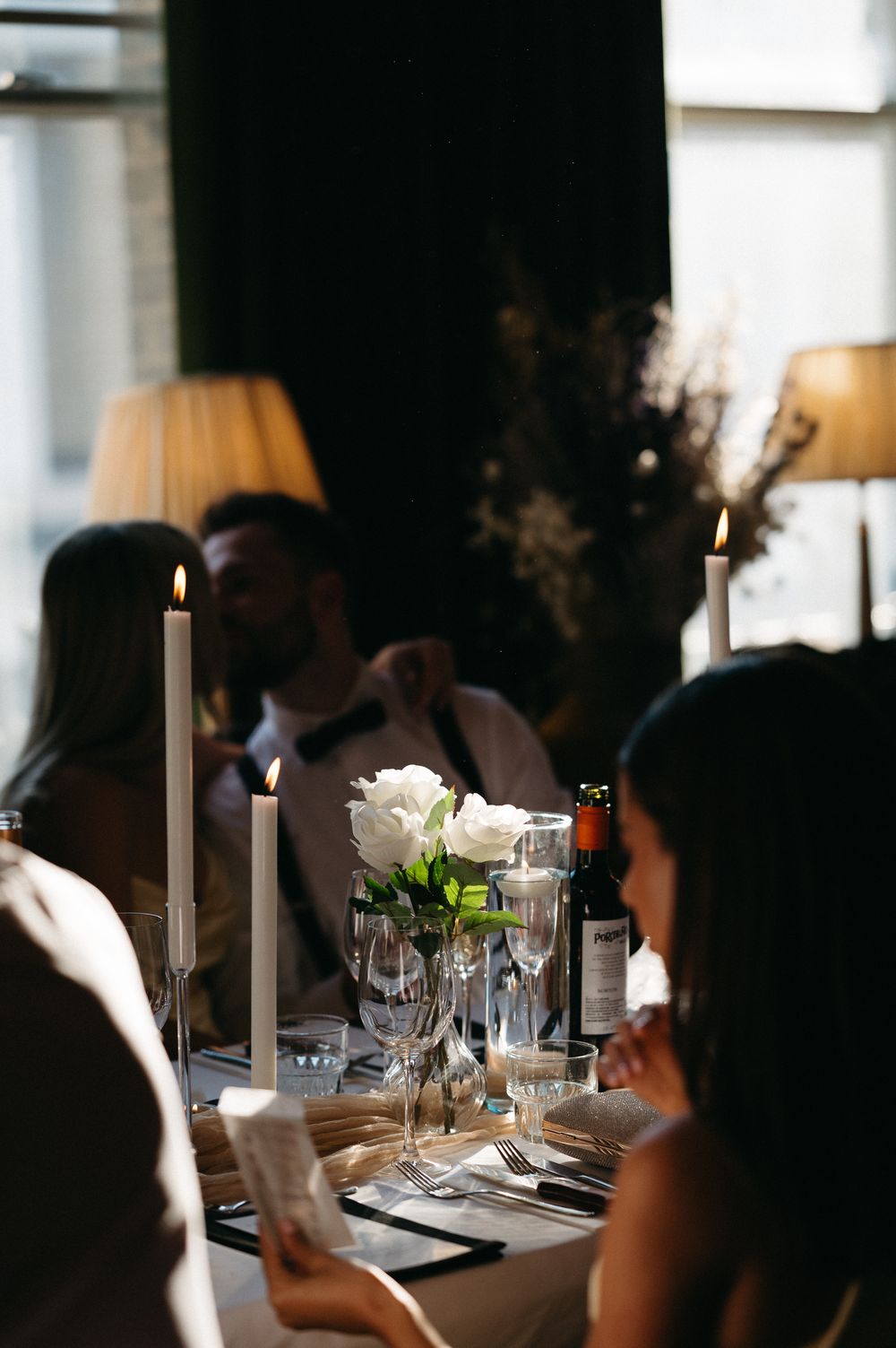 Table settings with glowing candles and white flowers create an elegant ambiance at wedding reception.
