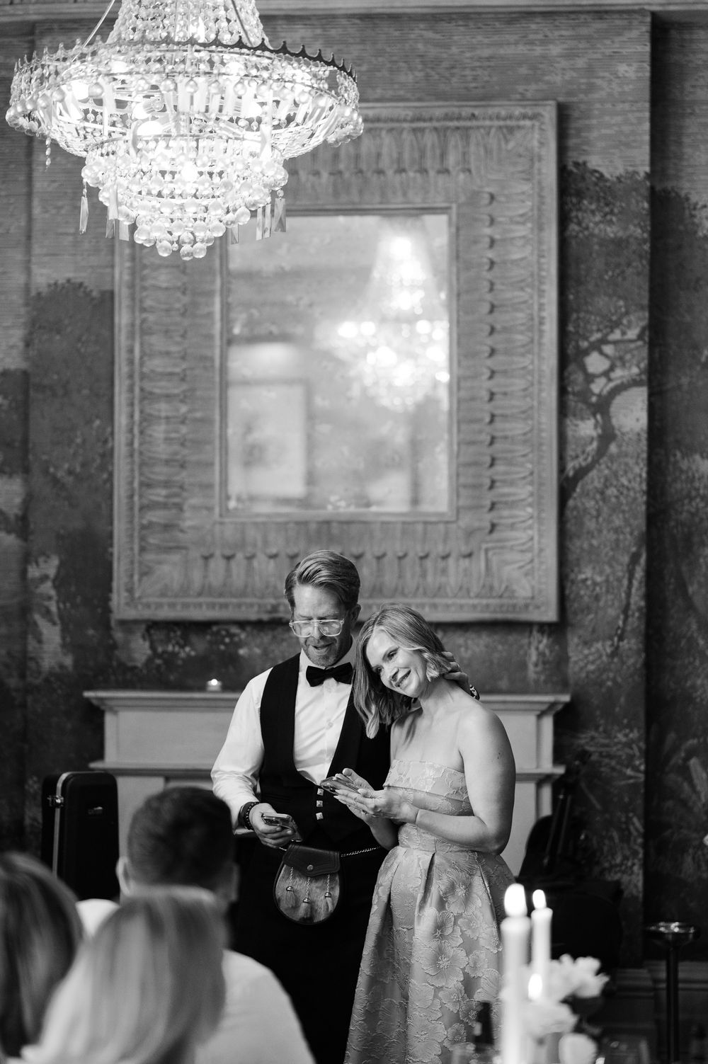 People celebrate at an elegant venue with crystal chandeliers and formal attire during an event reception.