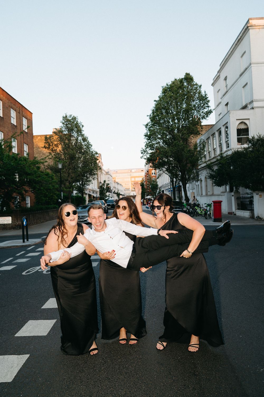 A group in black clothing perform playful seated poses on a city crosswalk at dusk.