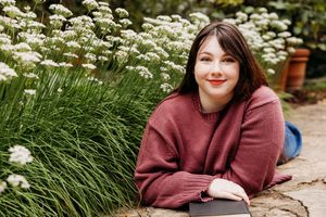 Someone in a burgundy sweater relaxes by a garden path surrounded by blooming white flowers and ornamental grasses.