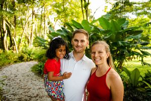 Family members pose together in front of lush tropical greenery in matching red and white attire.