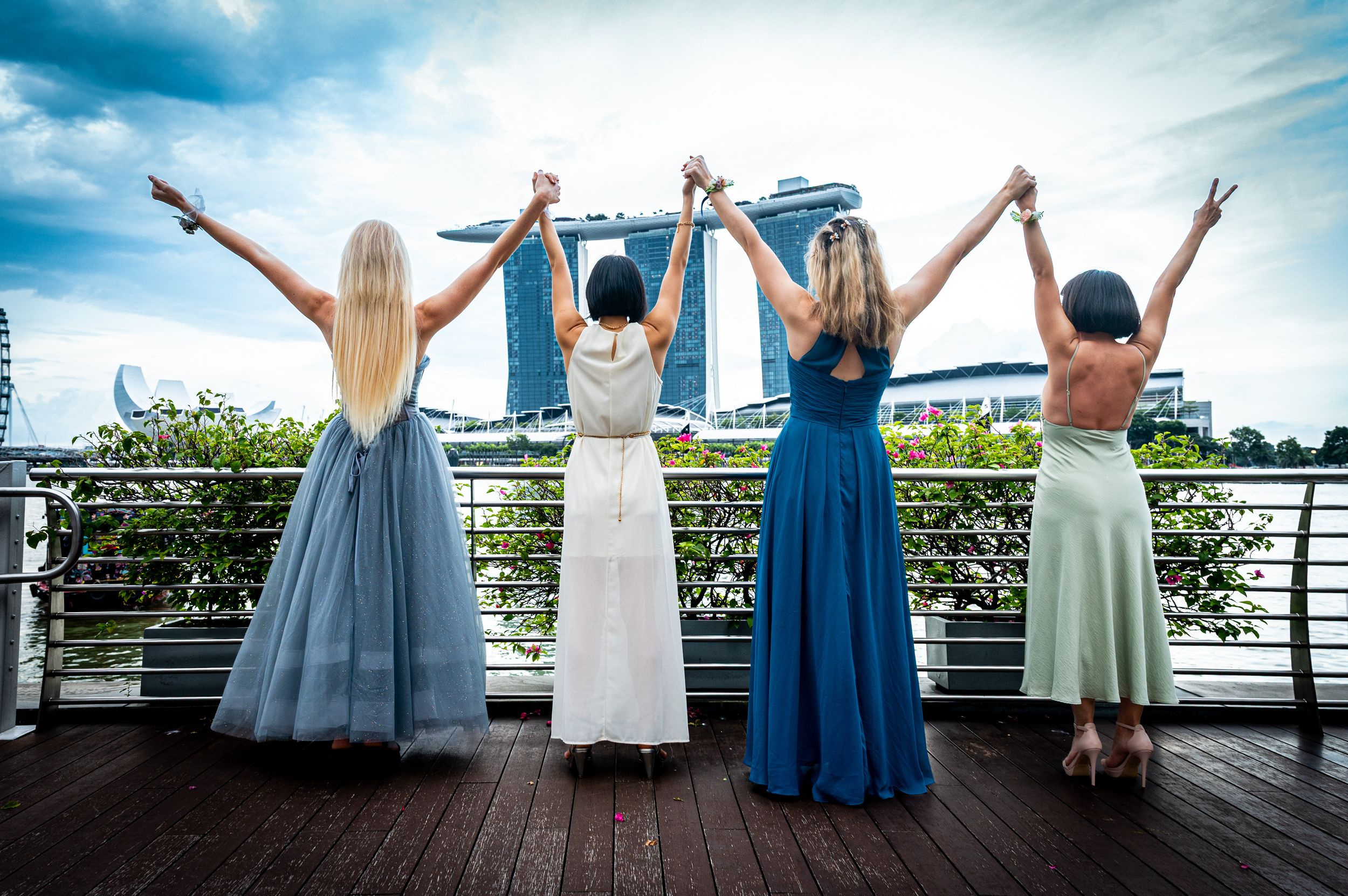 A group in blue and white dresses celebrating on a waterfront deck with their arms raised to the sky.