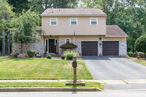 A two-story suburban home with tan siding, stone accents, two-car garage and landscaped front yard on a peaceful street.
