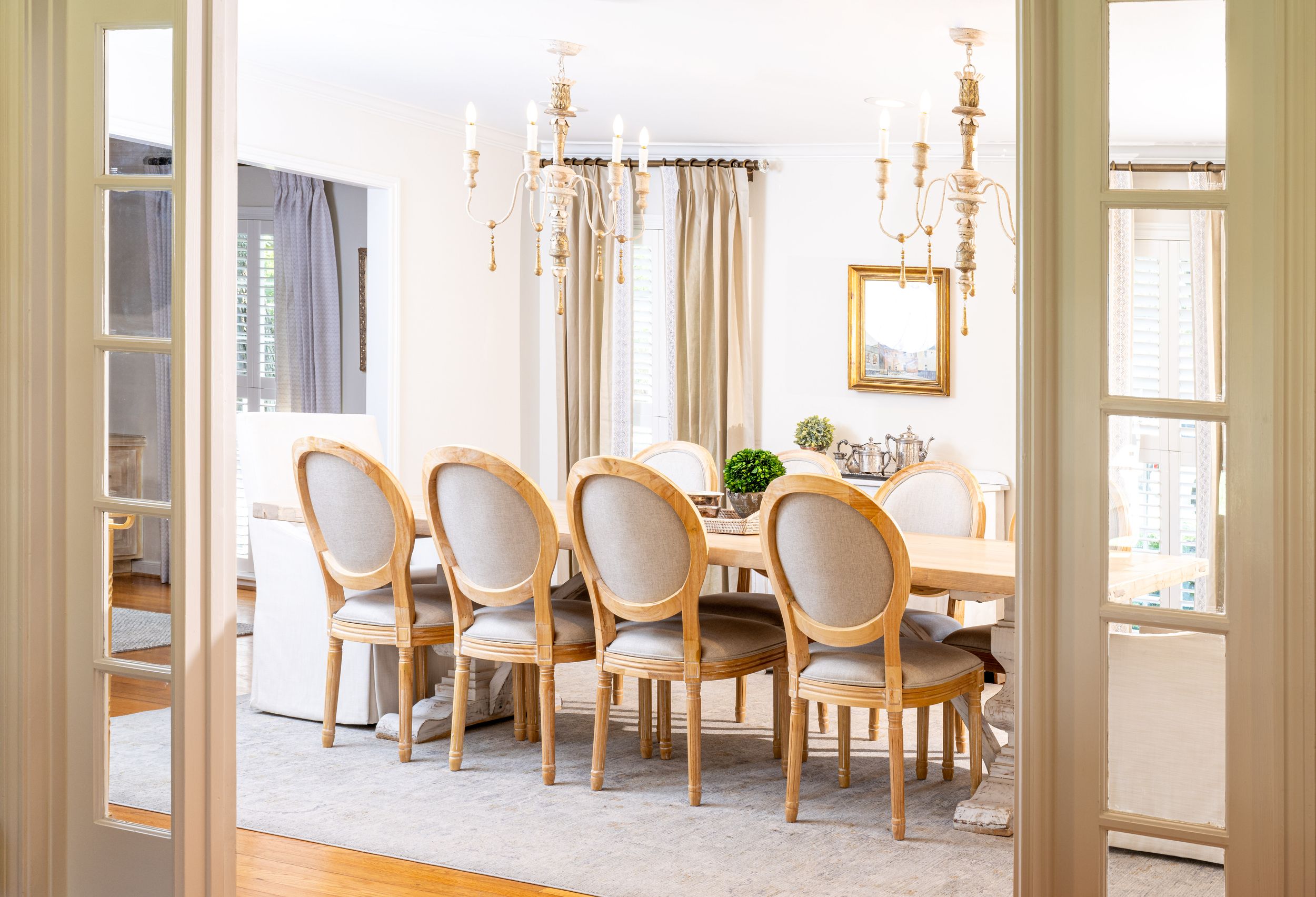 Elegant dining room with cream-colored oval back chairs and large windows in a bright, modern space.