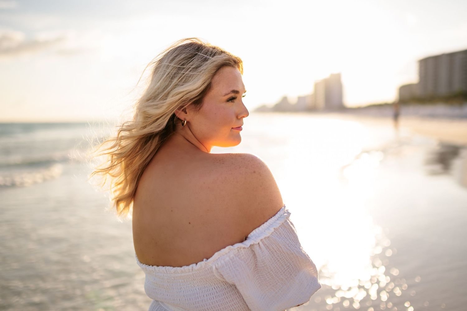 Sunlit beachfront scene with waves crashing and coastal buildings creating a romantic backdrop.