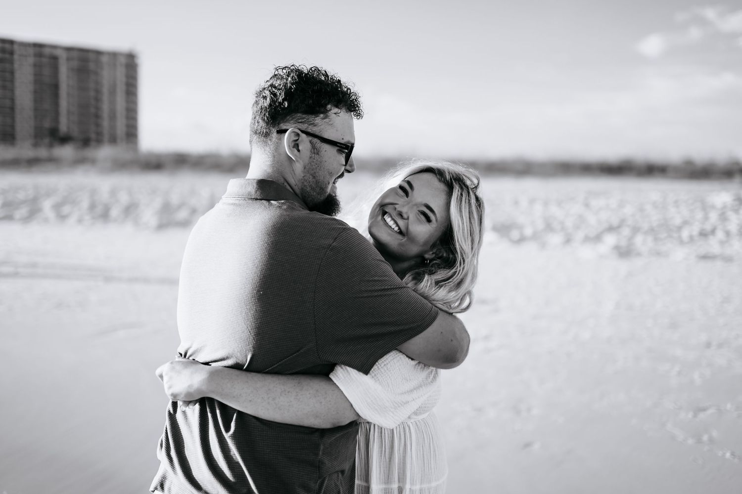 Black and white series of a couple sharing intimate moments on the beach with ocean backdrop.
