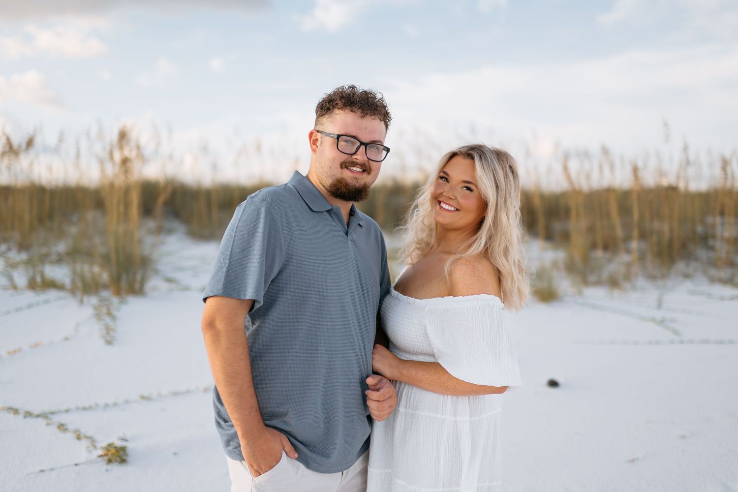 A couple shares a joyful moment together on white sand dunes during a beach photoshoot at sunset.