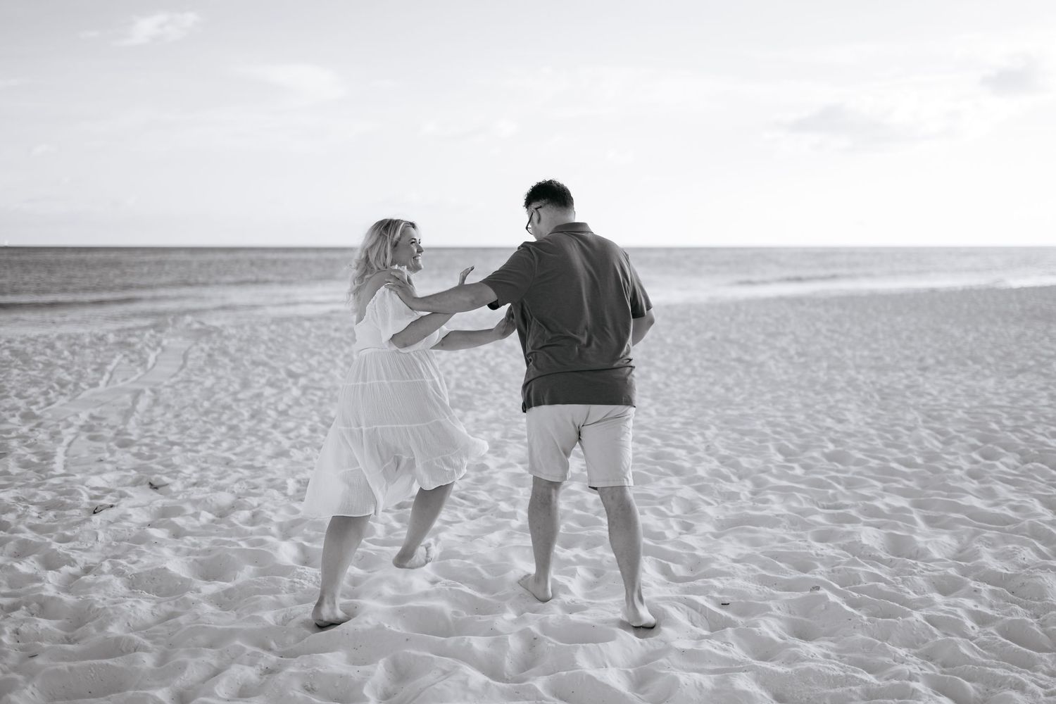 Couple walking together on a sandy beach at sunset with ocean waves in the background.