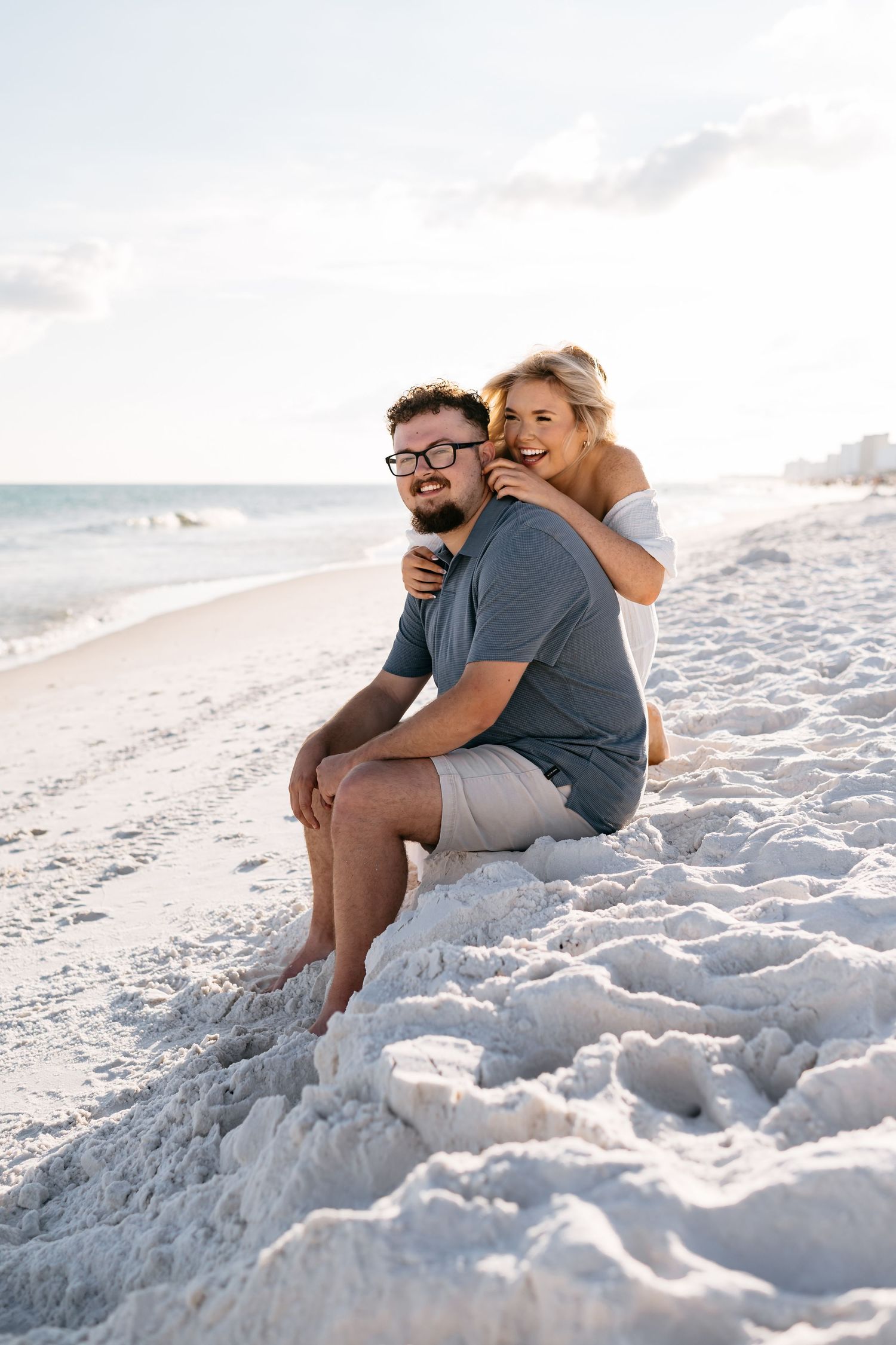 A romantic beach scene with a couple sitting together on pristine white sand by the ocean.