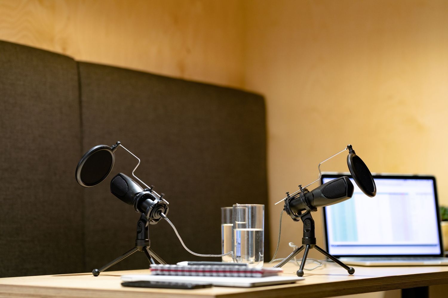 Professional podcast recording setup with microphones and laptops on a desk against a dark acoustic panel backdrop.