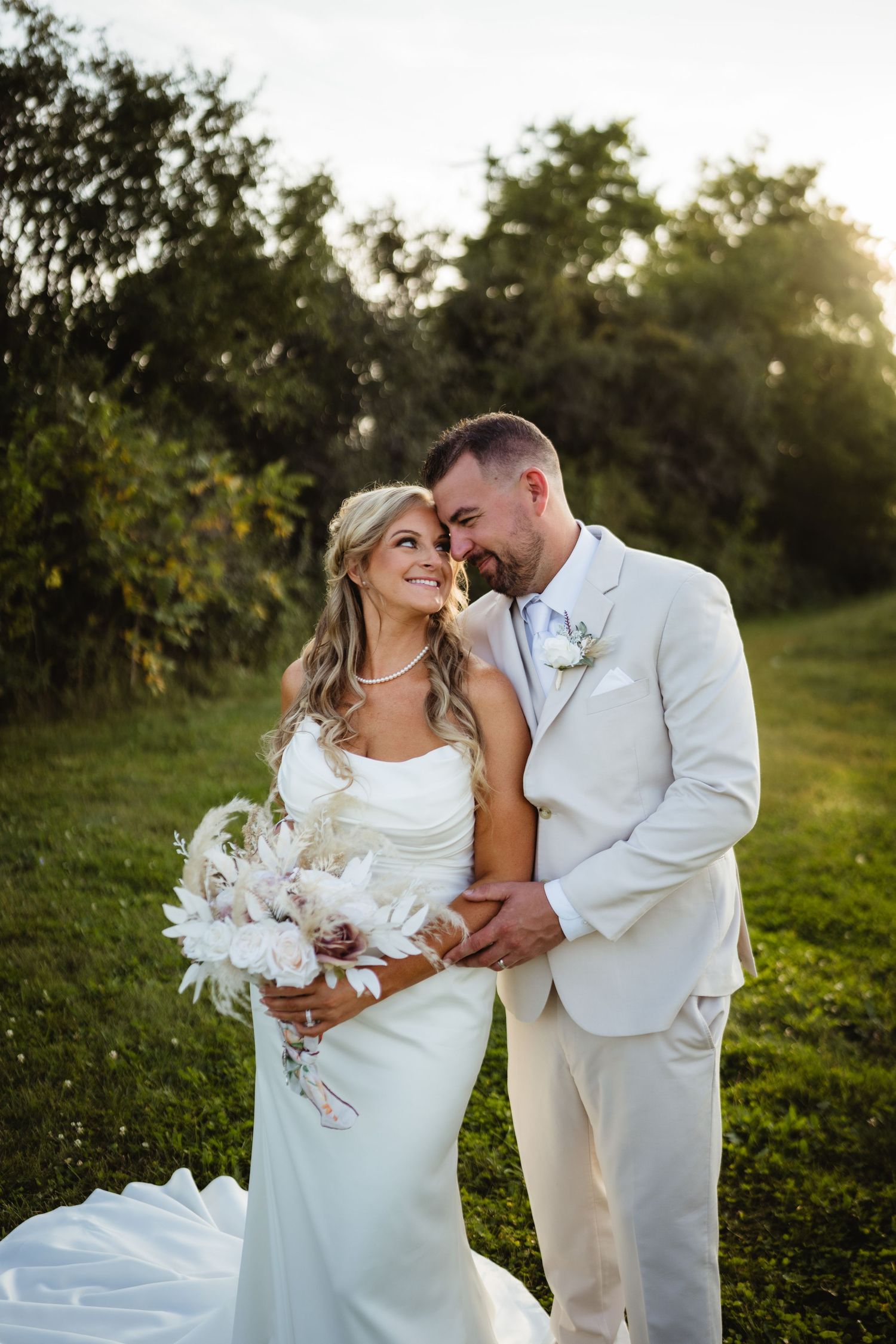 A couple sharing an intimate moment in a garden setting at sunset while wearing white wedding attire.