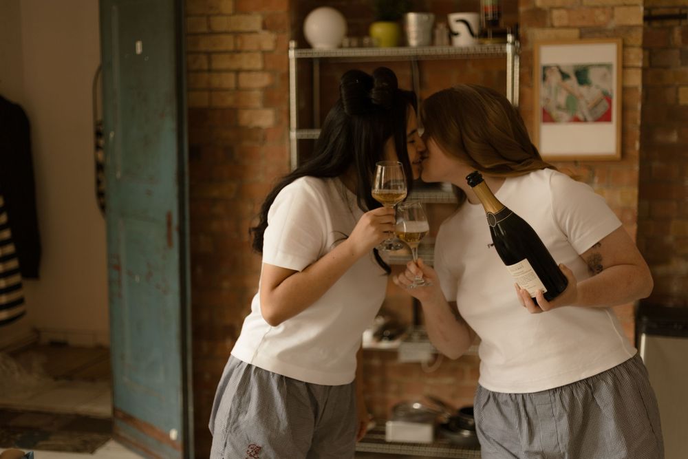 Two people wearing white shirts embrace in an intimate slow dance pose against a rustic brick wall interior.