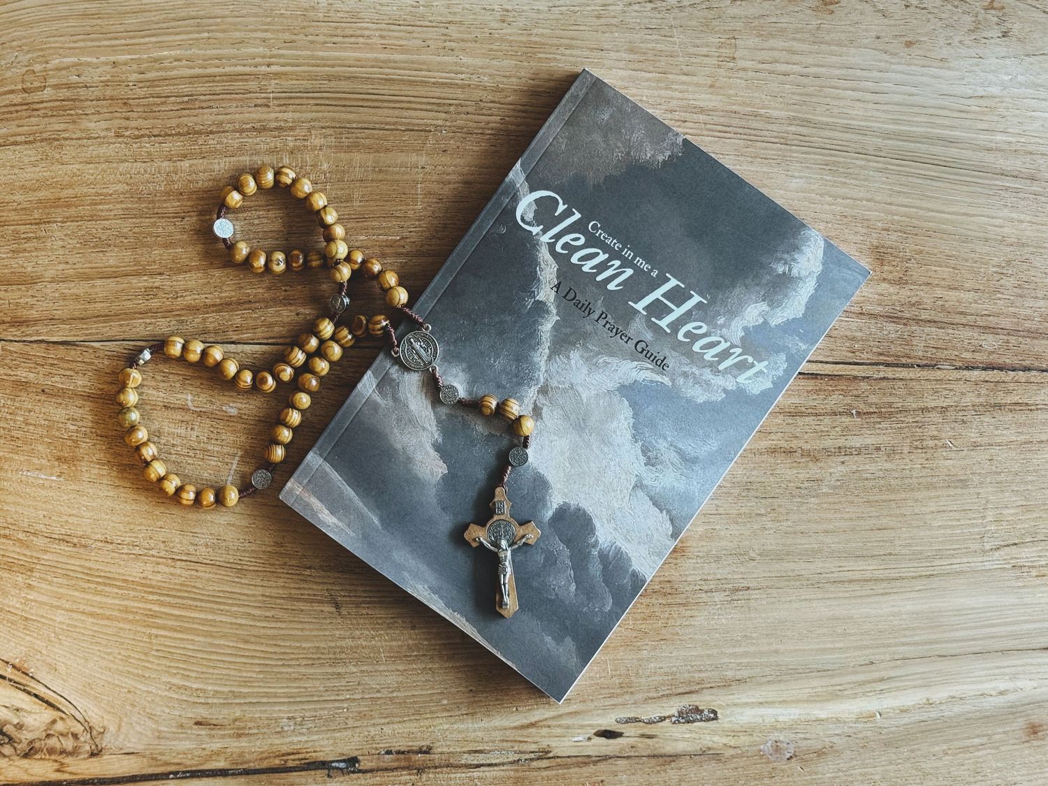 A gold beaded necklace lies next to a gray book cover on a light wooden surface.