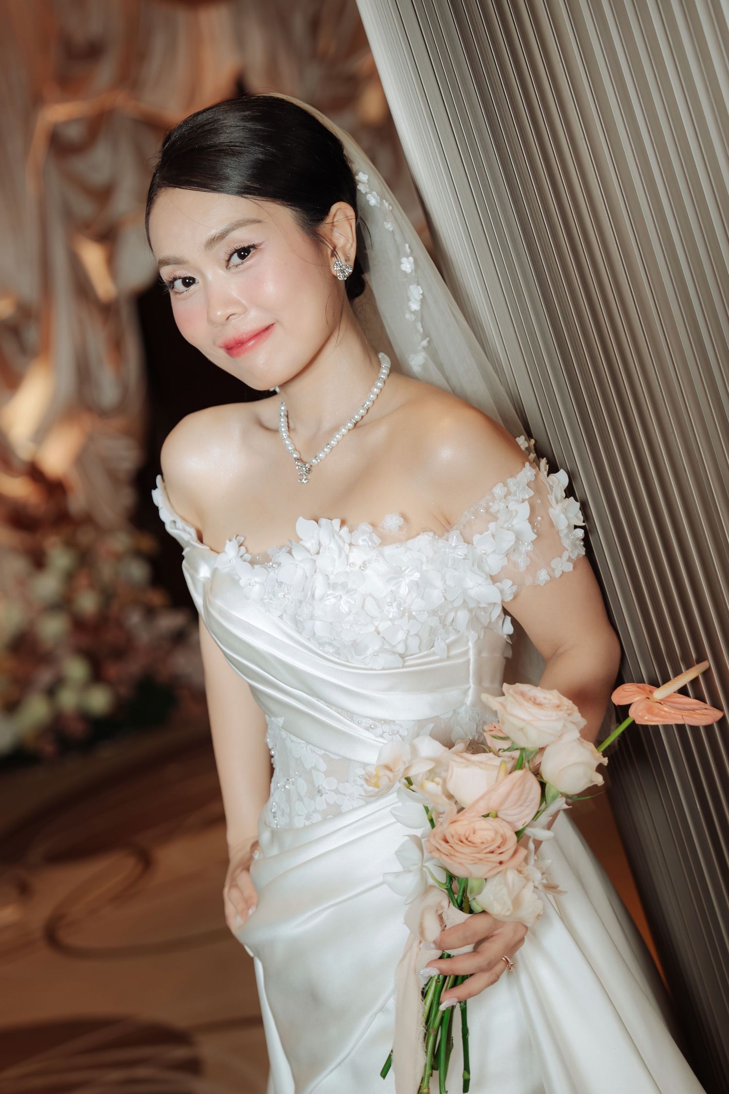 Beautiful bride in floral off-shoulder gown holds pink roses bouquet with diamond necklace.