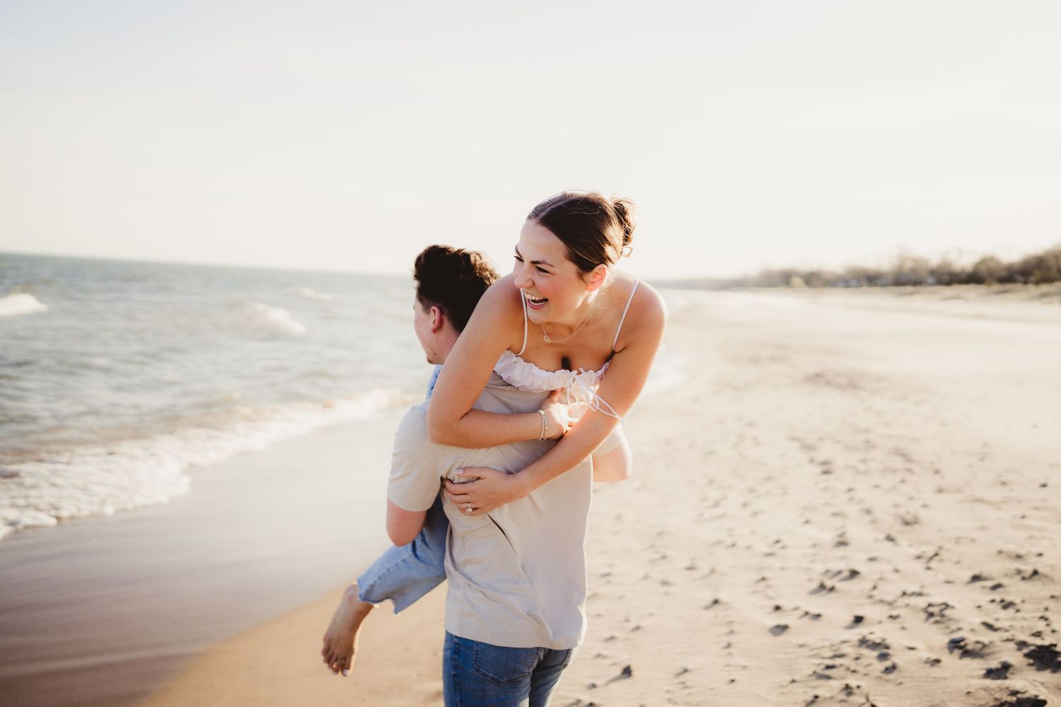 Two people sharing a playful moment while embracing on a sunny beach with ocean waves in the background.
