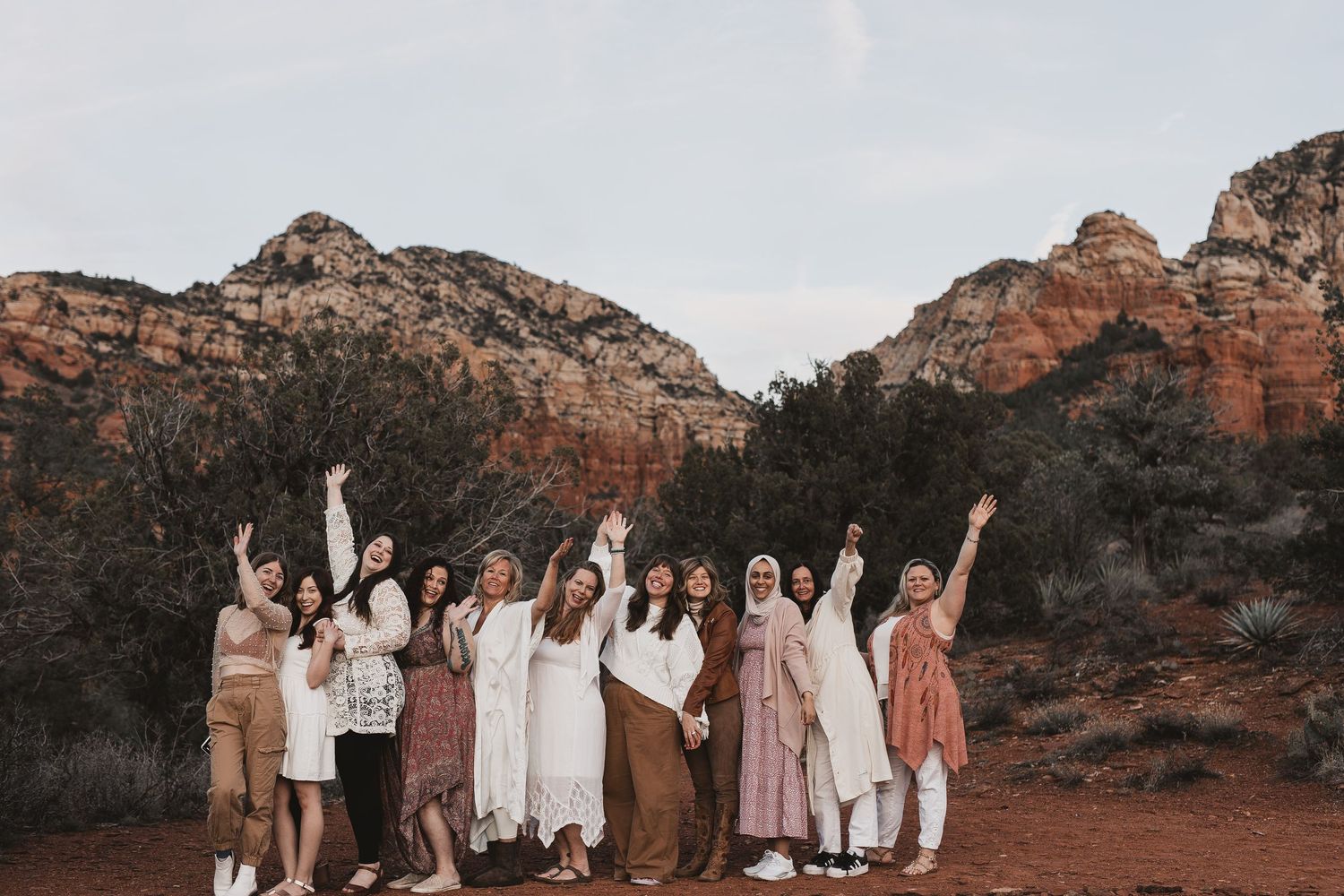 Group celebrates together while standing in front of majestic red rock formations at sunset.