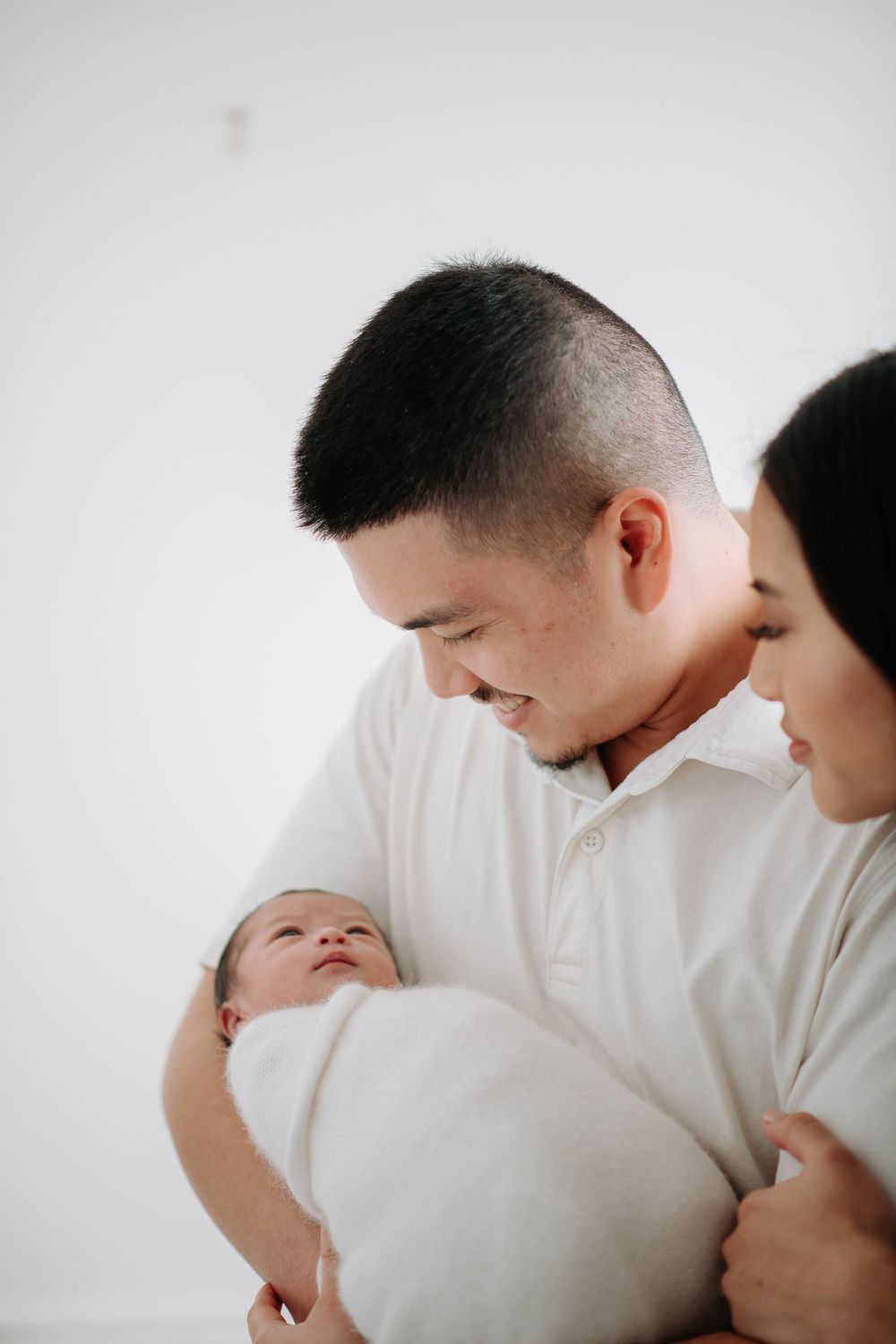 Tender family moment captured in white studio setting with newborn baby.