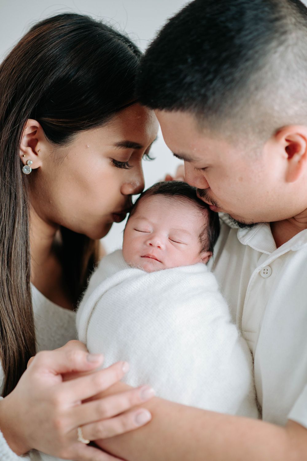 A tender family moment as parents share an intimate moment with their newborn baby wrapped in white.