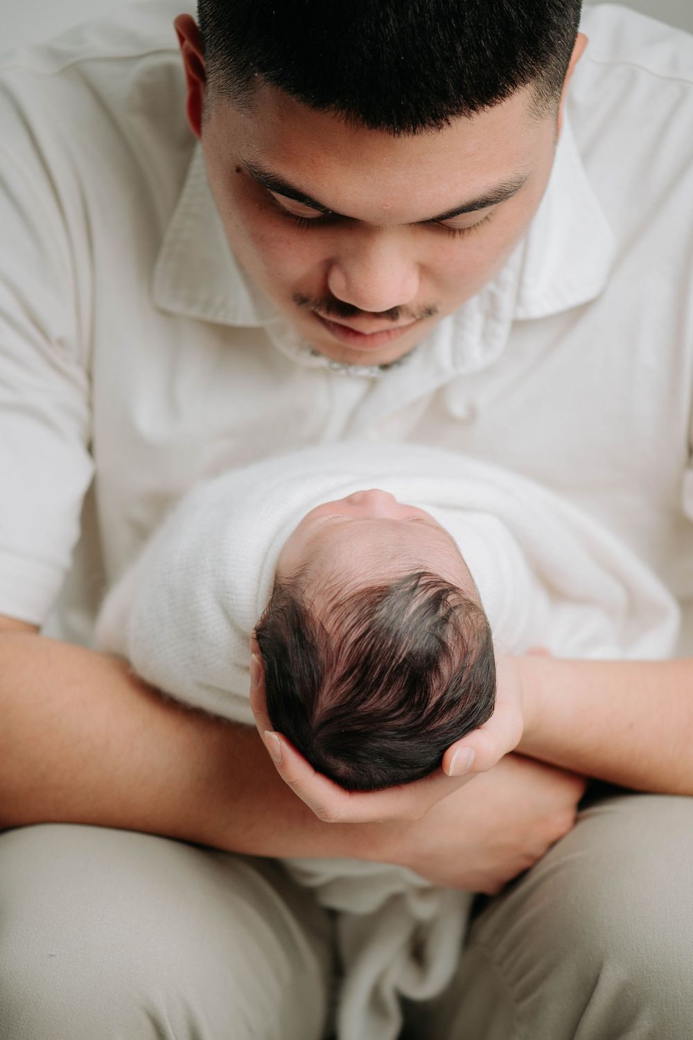 Close-up shots of parents cradling and bonding with their newborn baby in white setting.