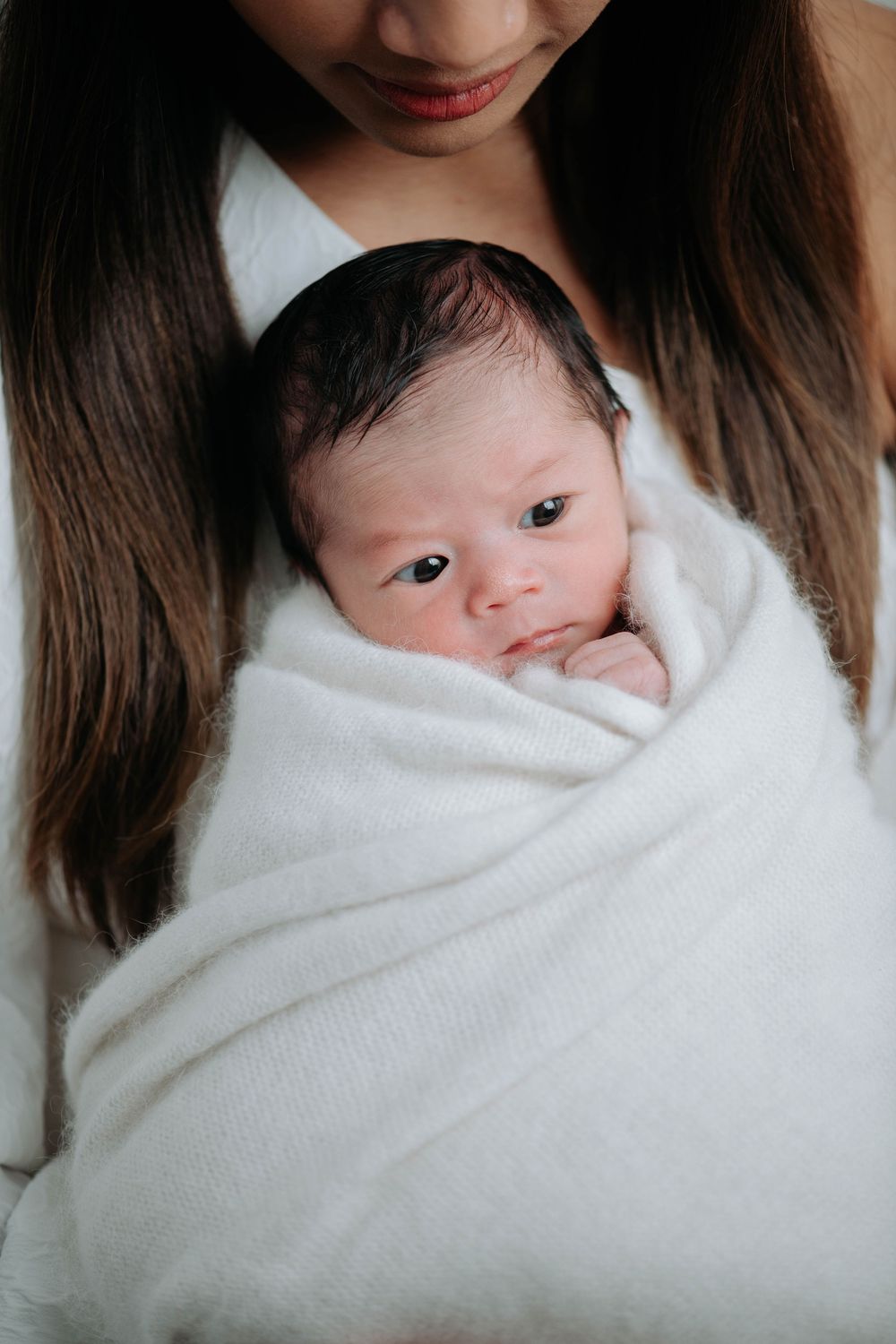 Close-up views of a newborn baby swaddled in a soft white blanket while being held by someone in white.