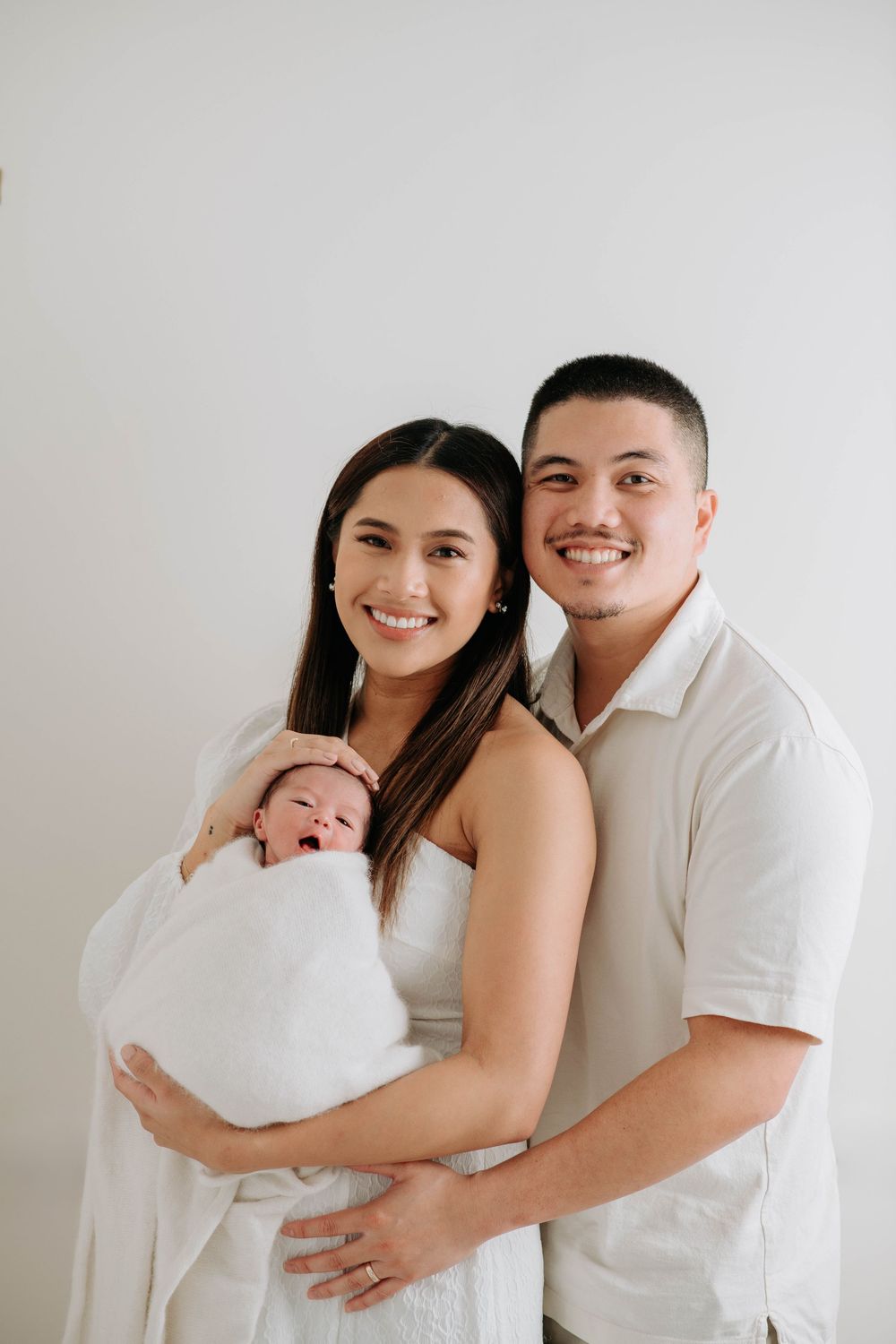Happy family of three poses in matching white outfits for studio portraits.
