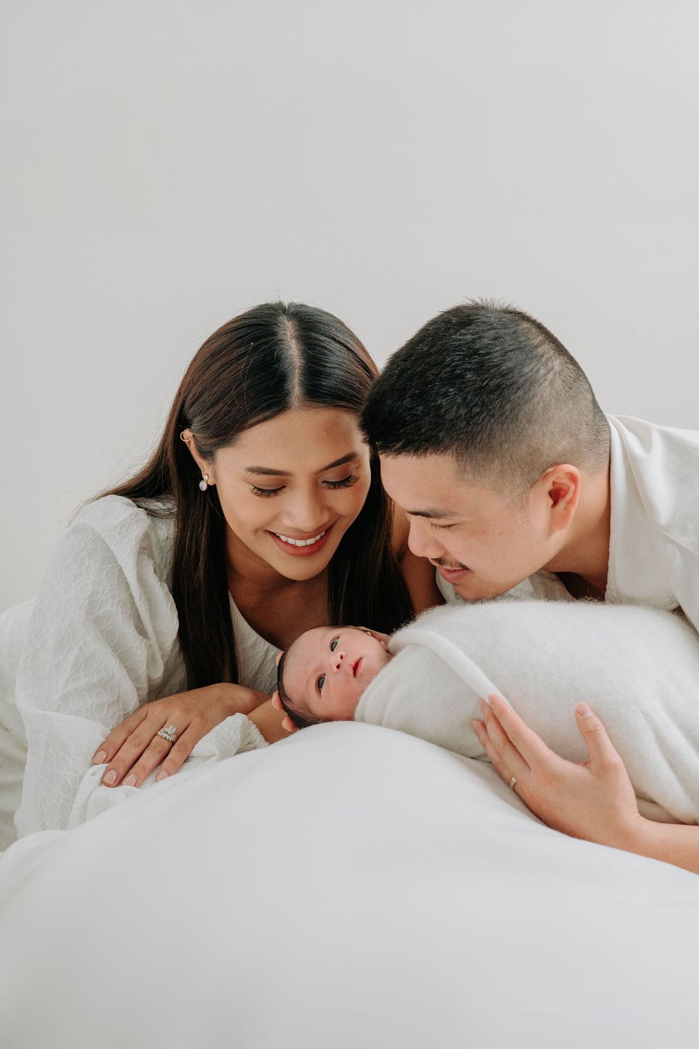 Happy parents sharing intimate family moment with newborn baby wrapped in white blanket.