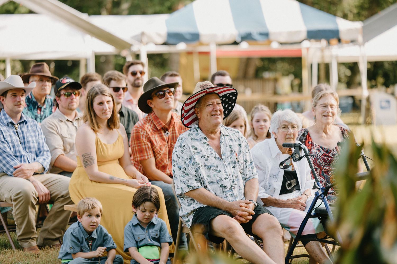 Diverse crowd of people sitting on chairs at an outdoor summer event watching a performance.