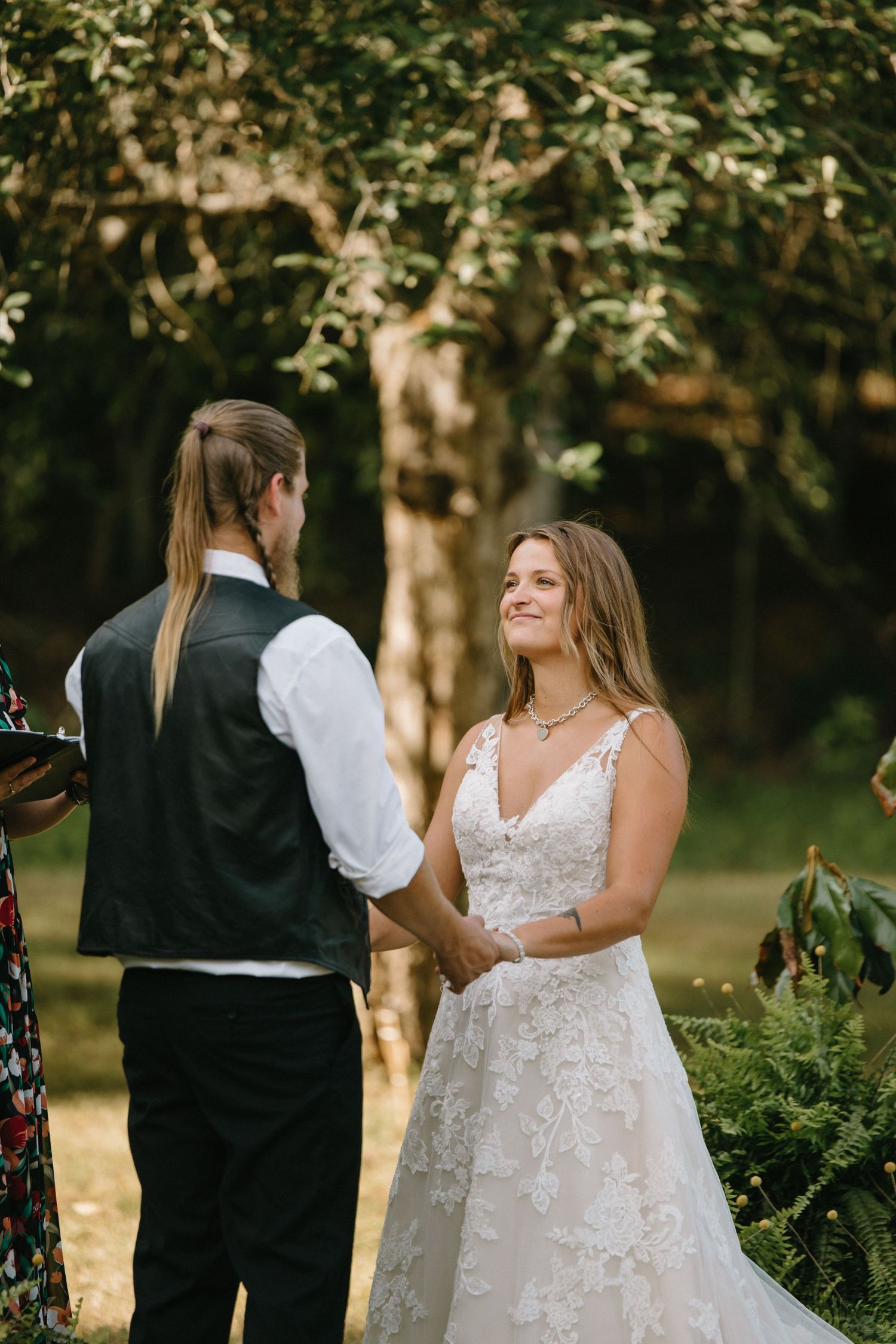 Joyous couple in formal wedding attire share candid laughing moments together in a sun-dappled garden setting.
