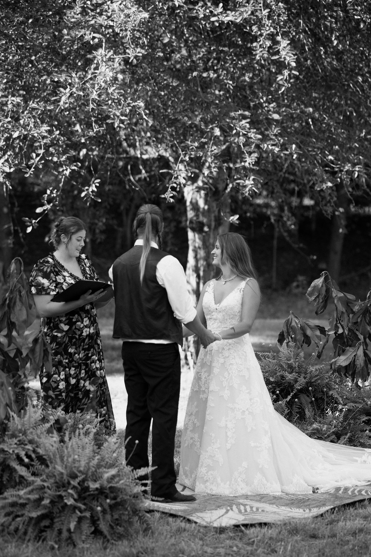 A wedding couple and their guests gather outdoors under blooming cherry trees in black and white photography.