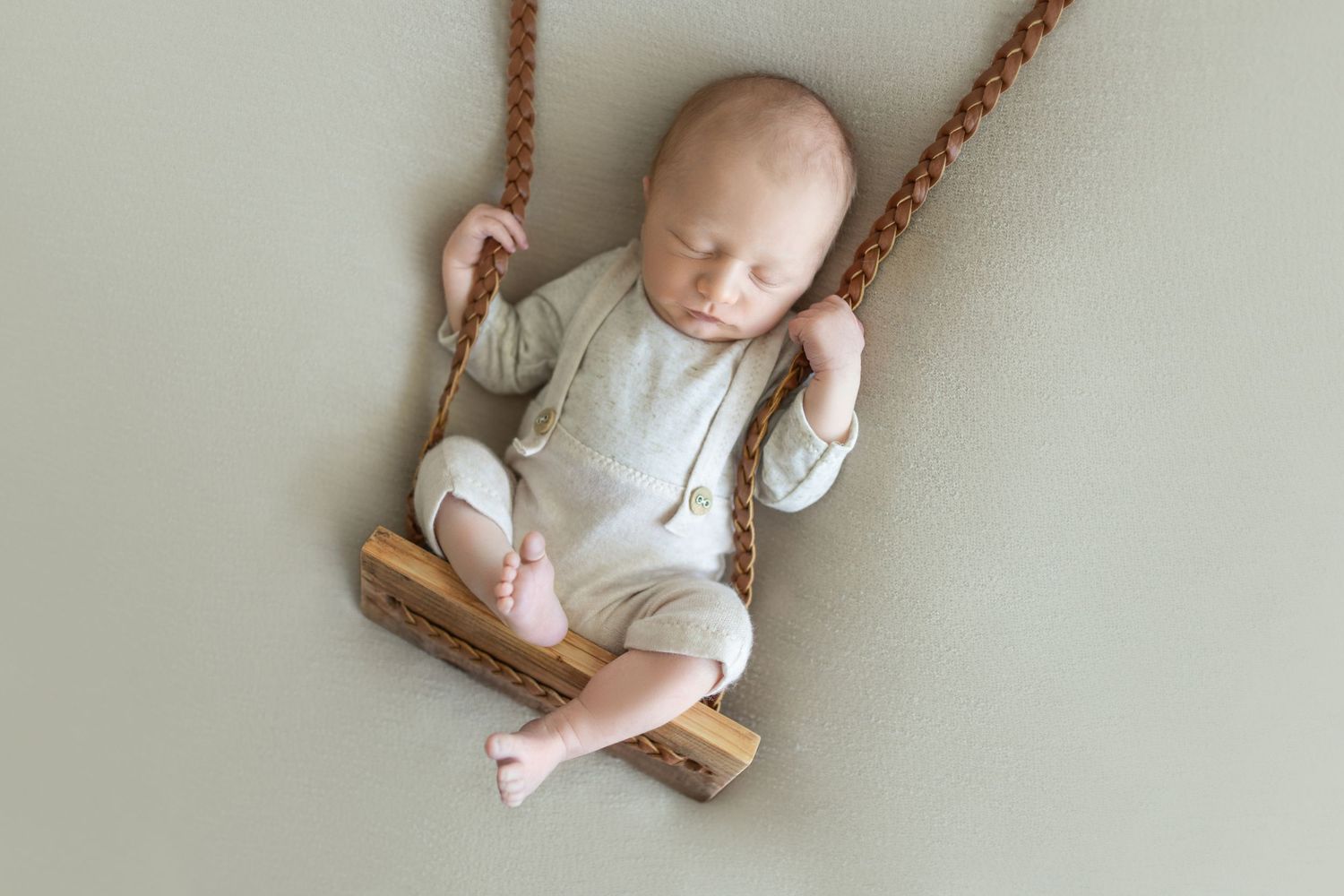 Baby photography series on a wooden swing against white background.