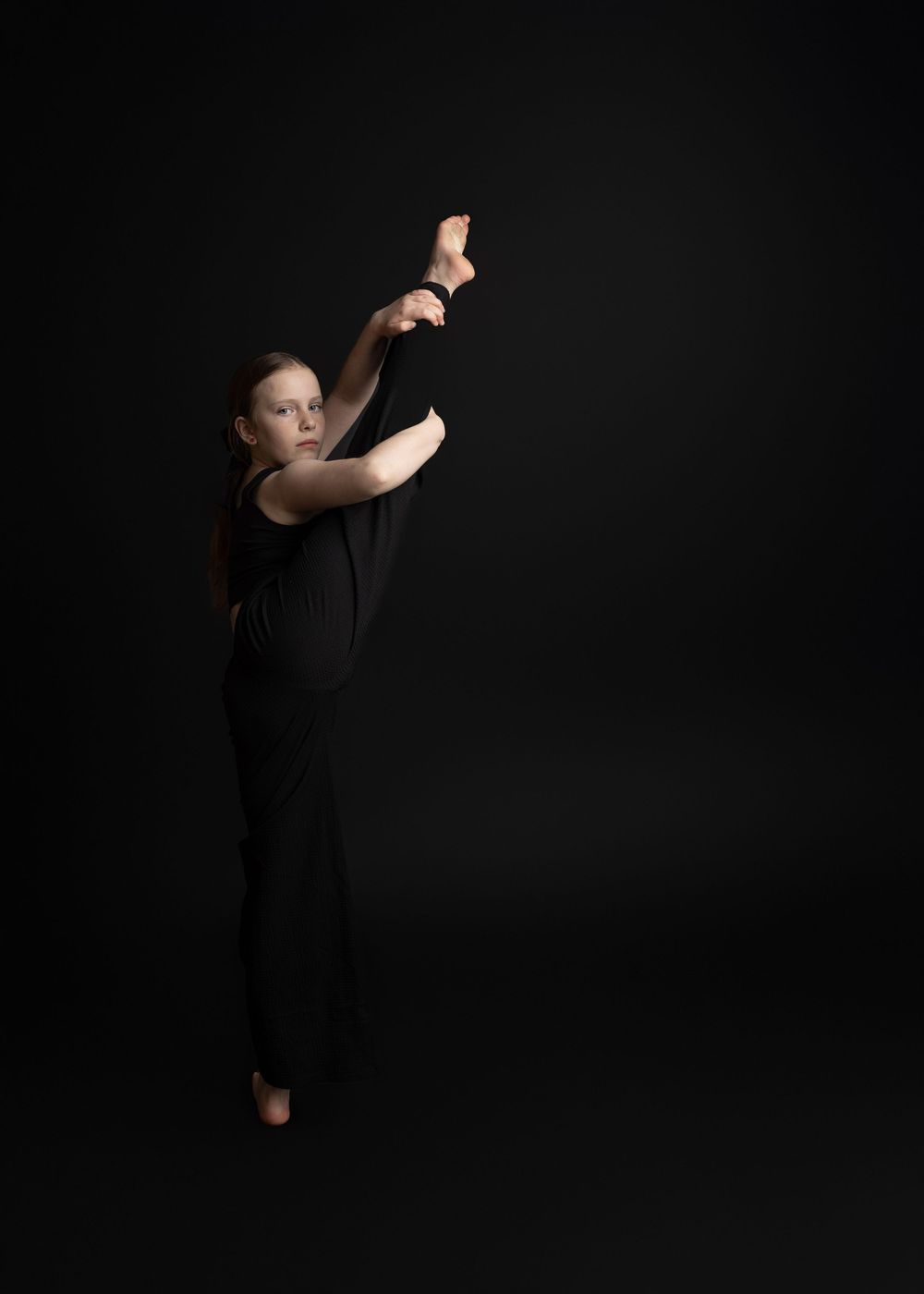 A dancer in a black outfit strikes an elegant pose against a dark background during a dramatic performance.