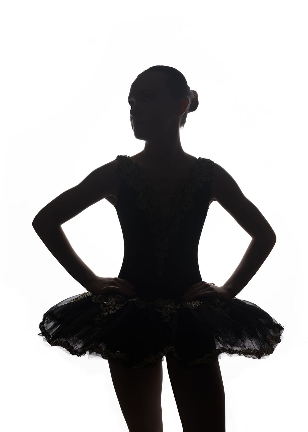 Dramatic silhouette of a ballet dancer in a tutu with hands on hips against white background.