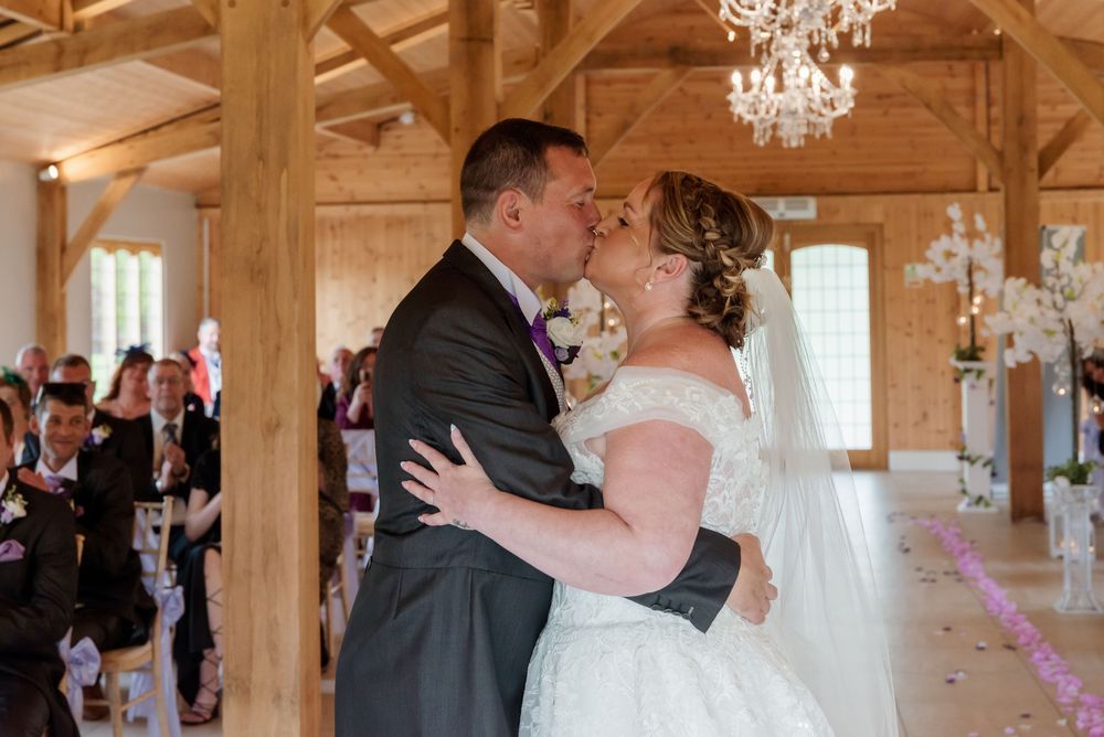 A romantic first dance moment in an elegant rustic barn venue with wooden beams and crystal chandelier overhead.