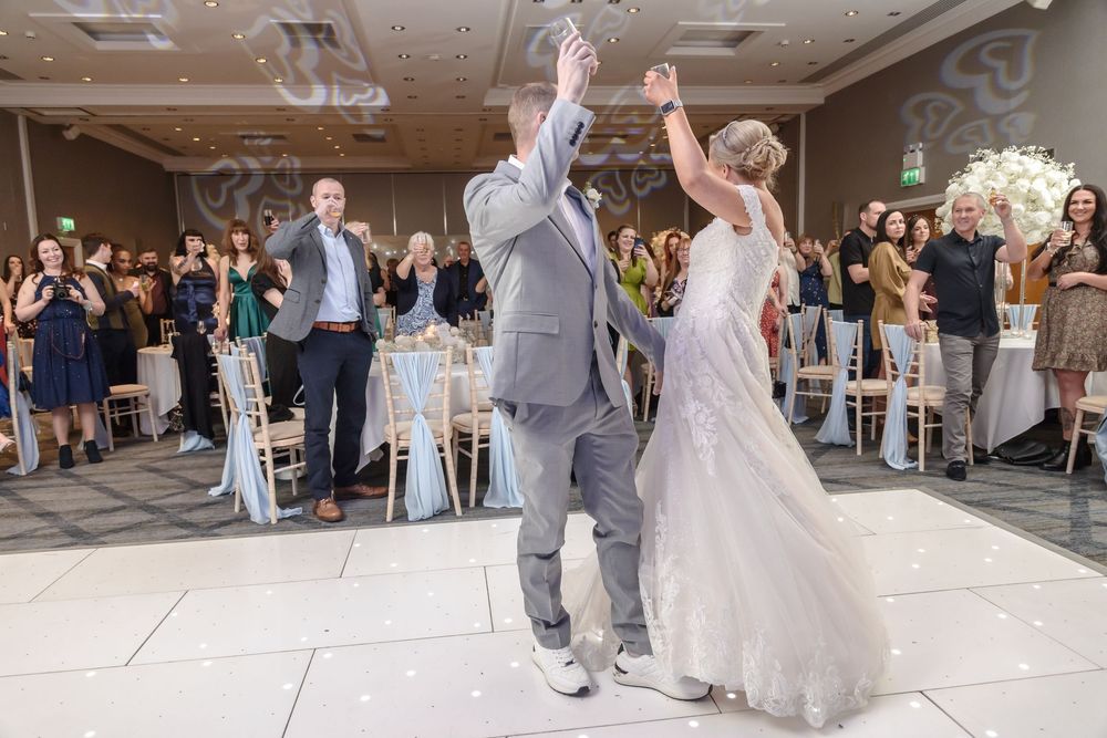 A bride and groom celebrate their first dance together at their wedding reception while guests watch and applaud.