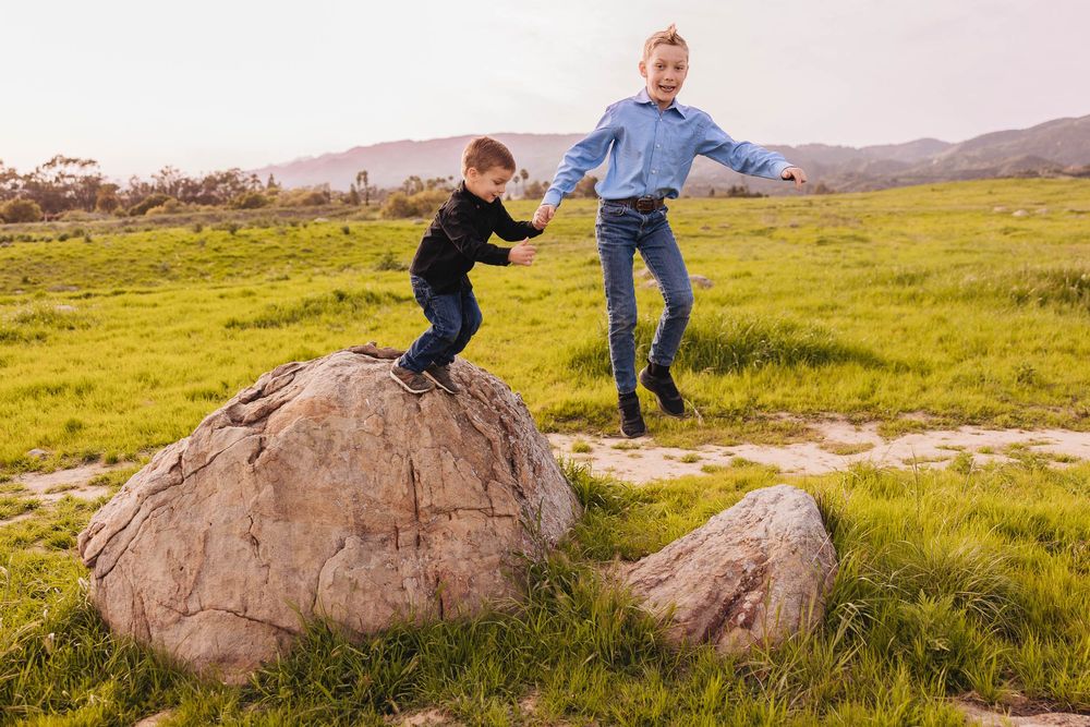 Children play and climb on large rocks in a grassy field at sunset.