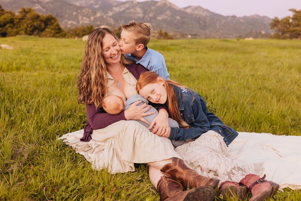 A couple shares tender moments while lying in a grassy field with mountains visible in the background.
