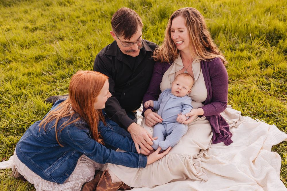 Family sitting on blanket in sunny field with baby during golden hour.